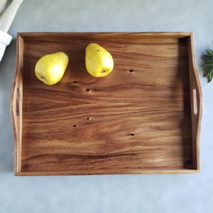 May include: A rectangular wooden serving tray with integrated handles. The tray is made of a warm-toned wood and features two yellow pears. The tray is ideal for serving food or as a decorative piece.