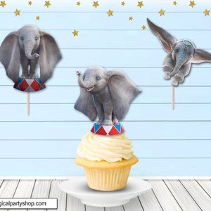May include: Three Dumbo cupcake toppers, each featuring a gray elephant with large ears. One topper shows Dumbo standing on a red, white, and blue circus ring. Another topper shows Dumbo flying with his ears outstretched. The third topper shows Dumbo standing on a cupcake with a red, white, and blue circus ring.