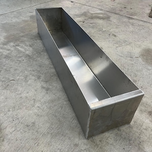 May include: A long, rectangular metal planter made of stainless steel. The planter is empty and has a smooth, reflective surface.