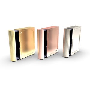 Puede incluir: Tres cajas met&aacute;licas con forma de libro en oro, cobre y plata. Cada caja tiene un lomo articulado y acanalado y una parte frontal rectangular con un borde decorativo. Las cajas est&aacute;n abiertas, revelando un interior oscuro.
