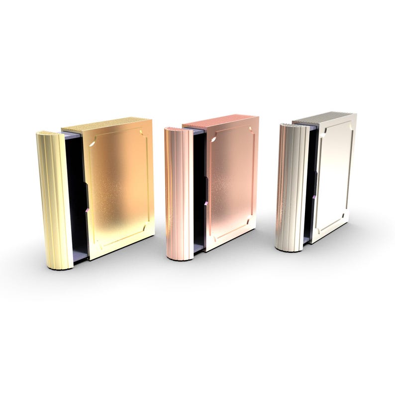 Puede incluir: Tres cajas met&aacute;licas con forma de libro en oro, cobre y plata. Cada caja tiene un lomo articulado y acanalado y una parte frontal rectangular con un borde decorativo. Las cajas est&aacute;n abiertas, revelando un interior oscuro.