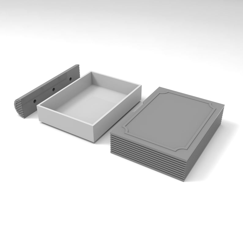 Puede incluir: Una caja rectangular gris, una pila de tarjetas grises y un objeto rectangular gris con agujeros. La caja est&aacute; abierta, revelando un interior blanco. Las tarjetas tienen un borde decorativo.