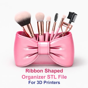 Puede incluir: Un organizador rosa en forma de lazo que contiene brochas de maquillaje, un rizador de pestañas y un peine de cejas. El organizador tiene un acabado brillante y el texto "Ribbon Shaped Organizer STL File For 3D Printers" se muestra debajo.