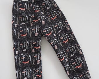 May include: Black pants with a woodland print featuring foxes, rabbits, and trees. The pants have an elastic waistband and cuffed legs.
