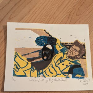 May include: A yellow, blue, and black linocut print of a person in a yellow and blue patterned shirt. The person is lying on their back with their arm outstretched and their hand holding a steering wheel. The print is titled "We're just getting started, babe" and is signed and dated 2024.