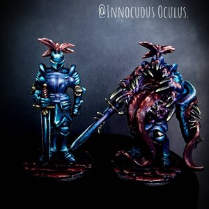 Op de afbeelding: Twee geschilderde miniatuurfiguren, de ene een blauwe ridder met een zwaard en de andere een monsterlijk wezen met tentakels en een zwaard. De figuren staan op ronde bases met een rood-zwart kleurenschema. "Painted Example by @INNOCUOUS_OCULUS." staat in witte tekst bovenaan de afbeelding.