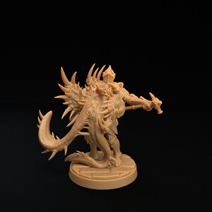 Op de afbeelding: Een gedetailleerd miniatuurbeeldje van een wezen met een stekelige staart en vleugels, dat een harnas draagt en een wapen vasthoudt. Het beeldje is in een lichtbruine kleur geverfd en staat op een ronde basis.