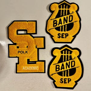 May include: Three yellow and black felt patches. One patch is a large letter "S" with the words "Polk" and "Academic" on it. The other two patches are a black lyre with the words "Band" and "Sep" on it.