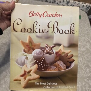 May include: A cookbook titled "Betty Crocker Cookie Book" with a cover image of various cookies, including star-shaped and flower-shaped cookies. The text "The Most Delicious Collection of Cookies Ever!" is also visible.