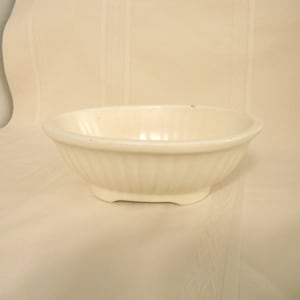 May include: A white ceramic bowl with a fluted design. The bowl is oval shaped and has a smooth, glossy finish.