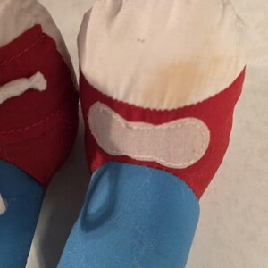 Peut inclure: Gros plan sur le pied et la jambe d'un jouet en peluche. Le pied est blanc avec une bordure rouge et un patch blanc. La jambe est bleue. Le jouet semble usag&eacute;, avec une certaine d&eacute;coloration.