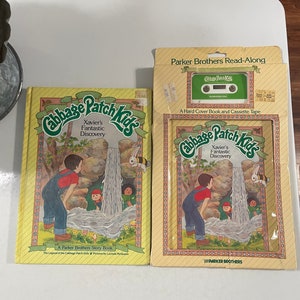 May include: A Cabbage Patch Kids book and cassette tape set featuring Xavier's Fantastic Discovery. The book has a yellow cover with illustrations of children playing by a waterfall. The cassette tape is green and has the Cabbage Patch Kids logo.