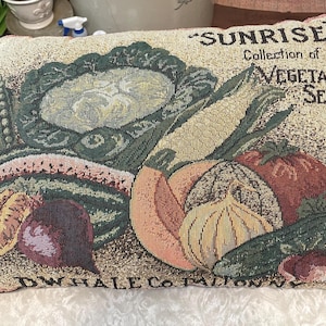 May include: Rectangular tapestry pillow featuring a colorful illustration of various vegetables, including corn, tomatoes, and onions. The pillow has the text "SUNRISE Collection of VEGETABLE SEEDS" and "DW HALE CO. TALLION NY".
