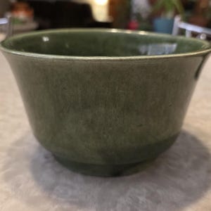 Peut inclure: Un bol en céramique vert avec un bord légèrement évasé. Le bol a une surface texturée et une base arrondie. La couleur est un vert sourd et terreux. Le bol est probablement utilisé pour servir ou exposer.