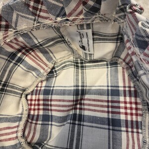 Peut inclure: Un panier en tissu à carreaux avec un bord à volants. Le panier présente un fond crème avec un motif de lignes bleues, rouges et noires. L'étiquette Longaberger Company est visible.