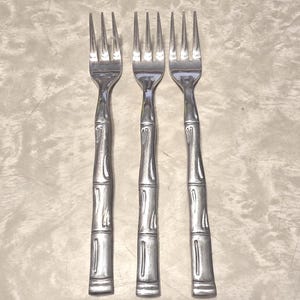 May include: Three silver-toned metal forks arranged vertically. Each fork features a handle designed with a textured pattern that mimics the segmented appearance of bamboo stalks, with three tines at the top of each utensil.