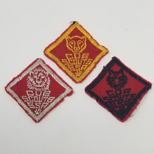 May include: Three embroidered patches in a diamond shape. One is red with a white lion design and text. Another is red with a yellow cat design and text. The third is red with a black wolf design and text. All have a white background.