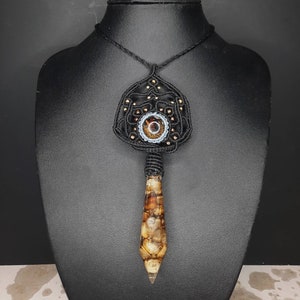 Peut inclure: Un collier en macramé noir avec un pendentif en agate brun et blanc. Le pendentif a la forme d'une larme et est orné de perles.