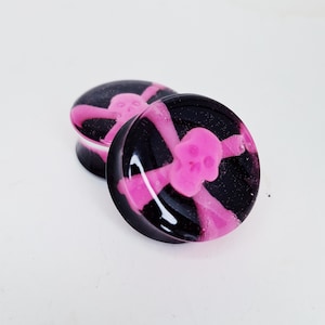 May include: Pair of black and pink glass ear gauges with a skull and crossbones design.
