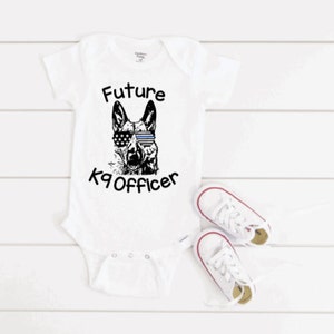 May include: White baby onesie with a black and white illustration of a dog wearing sunglasses and the text "Future K9 Officer".