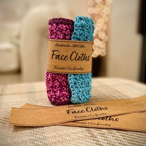 May include: Two handmade face cloths made from 100% cotton. The cloths are crocheted in a pink and blue pattern. The cloths are packaged with a brown paper label that reads "Handmade - 100% Cotton Face Cloths Reusable & Eco-friendly".