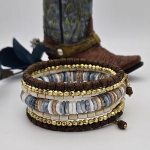 May include: A stack of six bracelets with brown, white, and blue beads. The bracelets are made of lava rock, wood, and ceramic beads.