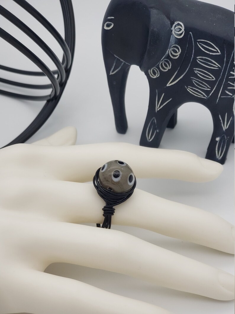 May include: A ring with a grey and black glass bead with white dots. The bead is wrapped with black wire.