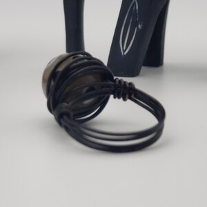 May include: A black wire wrapped ring with a brown stone. The ring is on a white surface.