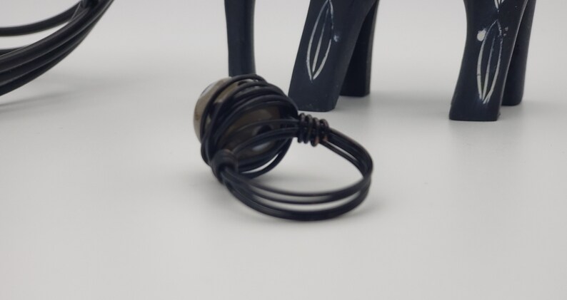 May include: A black wire wrapped ring with a brown stone. The ring is on a white surface.
