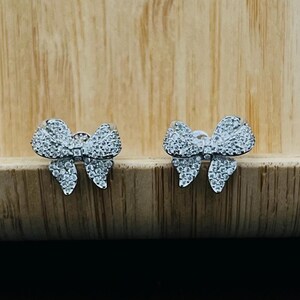 May include: A pair of silver bow-shaped earrings with clear cubic zirconia stones.