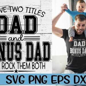 May include: A black and white graphic design with the text "I have two titles Dad and Bonus Dad and I rock them both". The graphic is on a white wood background. A man is holding a child on his shoulders. The child is wearing a blue shirt. The man is wearing a black t-shirt with the same graphic design in white.