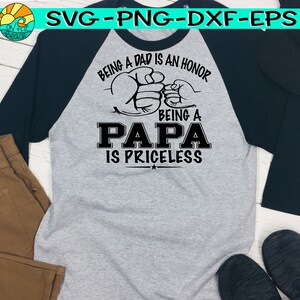 Puede incluir: Una camiseta de b&eacute;isbol gris y negra con el texto "Ser padre es un honor, ser pap&aacute; no tiene precio" y un gr&aacute;fico de dos manos entrelazadas.