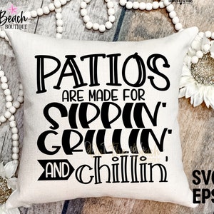 May include: A white pillow with black text that reads "Patios are made for sippin' grillin' and chillin'". The pillow is on a wooden surface with white beads and a white sunflower.