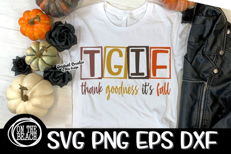 May include: A white t-shirt featuring the text "TGIF thank goodness it's fall" in a retro font. The letters are enclosed in boxes with autumnal colours. The shirt is displayed on a white surface with autumnal decorations.