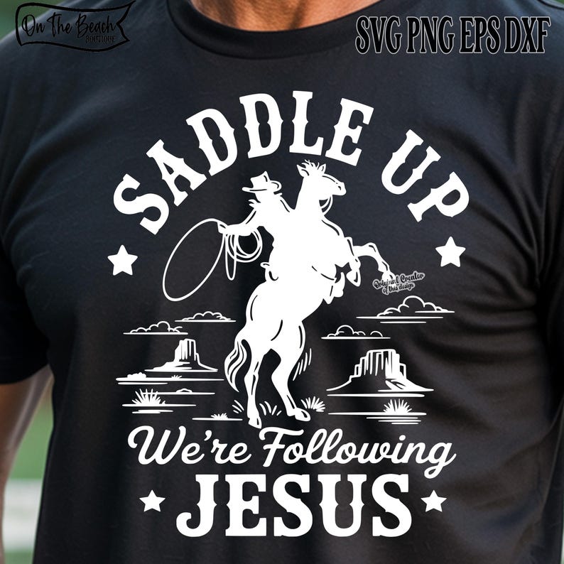 Peut inclure: T-shirt noir avec un motif blanc d'un cow-boy &agrave; cheval cabr&eacute;, lasso en main. Le texte "SADDLE UP" est au-dessus de l'image, avec "We're Following JESUS" en dessous. Des &eacute;toiles et des &eacute;l&eacute;ments de paysage d&eacute;sertique compl&egrave;tent le design.