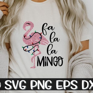 Puede incluir: Camiseta blanca con un flamenco rosa brillante decorado con luces navideñas. El texto "fa la la la MINGO" está escrito en escritura negra. La parte inferior de la imagen tiene el texto "SVG PNG EPS DXF".