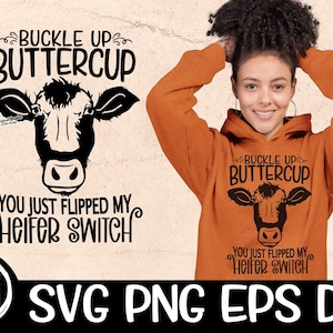 May include: A black and white graphic design featuring a cow's head with the text "Buckle Up Buttercup You Just Flipped My Heifer Switch". The design is on a light brown background with a white circle with the text "On The Beach" in black.