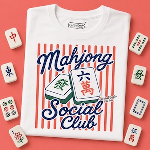 May include: White t-shirt with a red and white striped design. The shirt features the words "Mahjong Social Club" in blue script, along with two Mahjong tiles. Several Mahjong tiles surround the shirt.