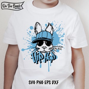 K&ouml;nnte beinhalten: Ein wei&szlig;es T-Shirt mit einer blauen und schwarzen Grafik eines Kaninchens, das eine Sonnenbrille und einen Hut tr&auml;gt. Das Kaninchen ist von blauen Farbflecken umgeben und das Wort "Hip Hop" ist darunter geschrieben. Der Text "Original Creator of this design" ist ebenfalls enthalten.