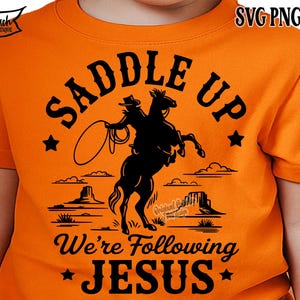 Peut inclure: T-shirt orange avec un motif noir d'un cowboy sur un cheval cabr&eacute;, lan&ccedil;ant un lasso. Le texte "SADDLE UP" est au-dessus, et "We're Following JESUS" en dessous. &Eacute;toiles et paysage d&eacute;sertique compl&egrave;tent le design.