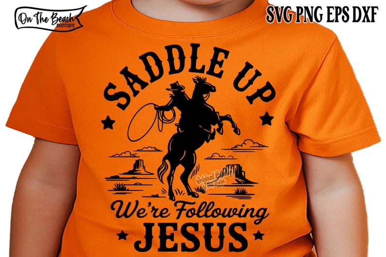 Peut inclure: T-shirt orange avec un motif noir d'un cowboy sur un cheval cabr&eacute;, lan&ccedil;ant un lasso. Le texte "SADDLE UP" est au-dessus, et "We're Following JESUS" en dessous. &Eacute;toiles et paysage d&eacute;sertique compl&egrave;tent le design.