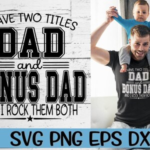 May include: A black and white graphic design with the text "I have two titles Dad and Bonus Dad and I rock them both". The graphic is on a white wood background. A man is holding a child on his shoulders. The child is wearing a blue shirt. The man is wearing a black t-shirt with the same graphic design in white.
