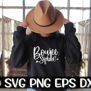 Può includere: Una felpa nera con la scritta "Boujee Squad" in lettere bianche. La felpa è indossata da una persona che indossa un fedora marrone.