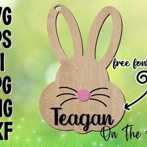 May include: A wooden cutout of a bunny rabbit with a pink nose and black whiskers. The bunny's ears are large and floppy. The name "Teagan" is written below the bunny's face, and the text "On The Beach Boutique" is written below the name.