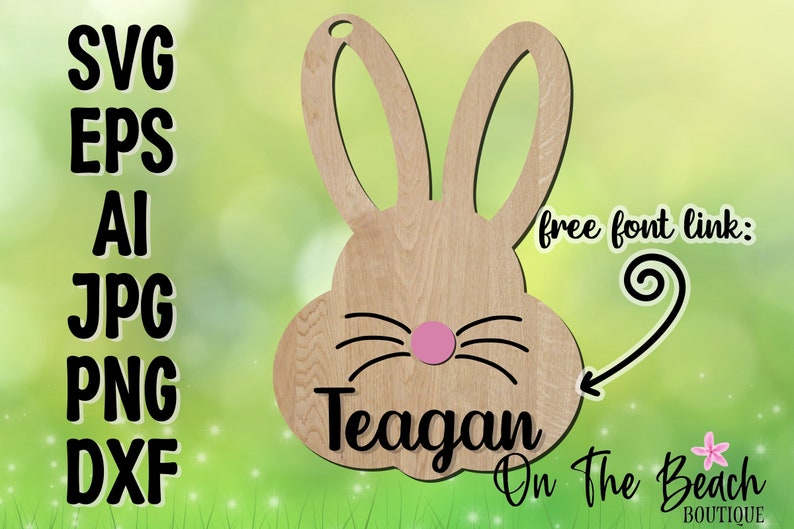 May include: A wooden cutout of a bunny rabbit with a pink nose and black whiskers. The bunny's ears are large and floppy. The name "Teagan" is written below the bunny's face, and the text "On The Beach Boutique" is written below the name.