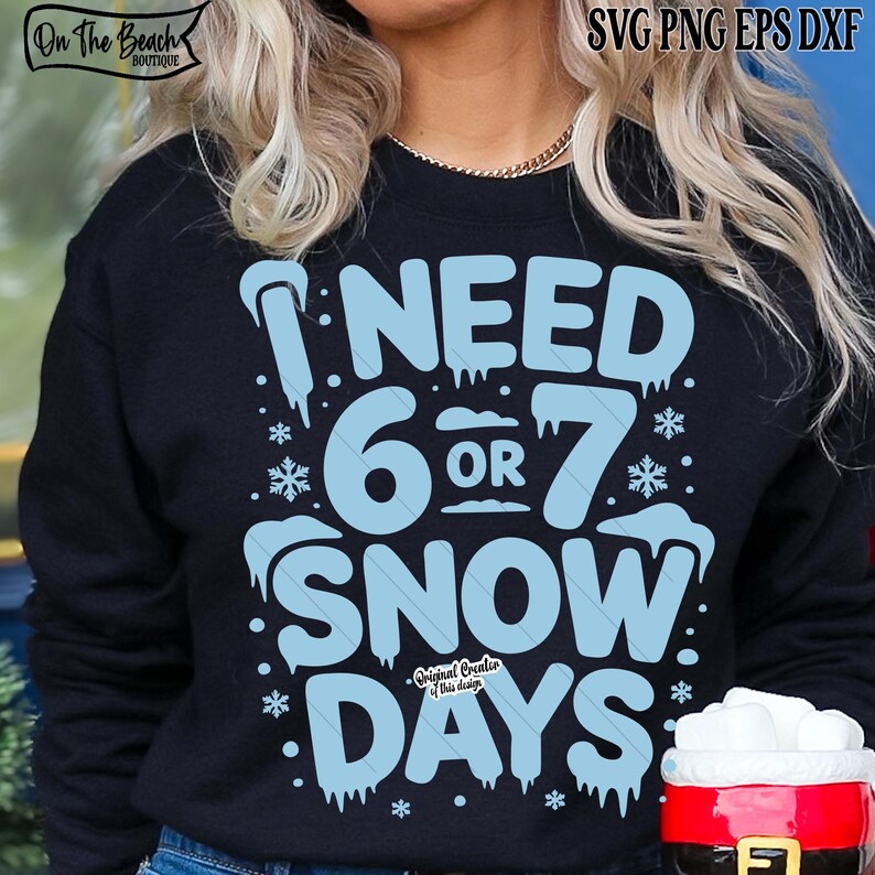 May include: A navy blue sweatshirt with the text "I NEED 6 OR 7 SNOW DAYS" in light blue. The design includes snowflakes and icicles. The sweatshirt has the text "On The Beach Boutique" at the top left.