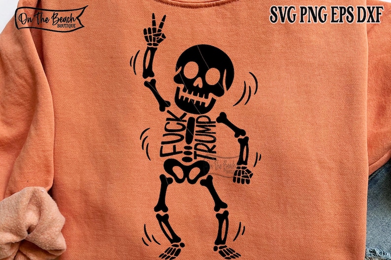 Op de afbeelding: Oranje sweatshirt met een zwart skeletontwerp. Het skelet maakt een vredesteken en heeft de woorden "FUCK TRUMP" op zijn ribbenkast gedrukt. Het sweatshirt heeft ook de tekst "SVG PNG EPS DXF".