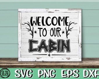 May include: White wooden sign with black text that reads "Welcome to our Cabin". The sign has a distressed look and features two stylised branches with leaves on either side of the text.