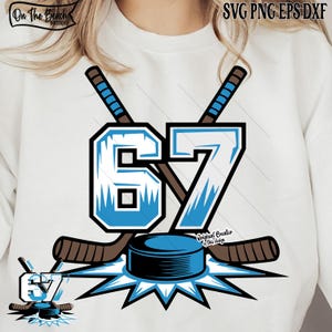 May include: A white sweatshirt design with a hockey theme. The design features the number 67 in light blue with a black outline, two crossed hockey sticks, and a hockey puck. The text "On The Beach Boutique" and "Original Creator of this design" are also present.