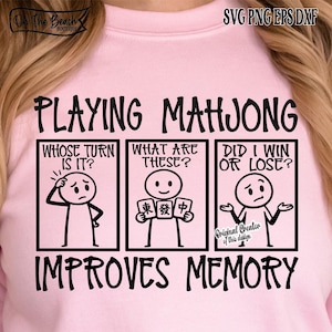 May include: Pink sweatshirt with a black graphic design. The design features the text "PLAYING MAHJONG IMPROVES MEMORY" with stick figures and questions about the game. The top left corner has the text "On The Beach Boutique".